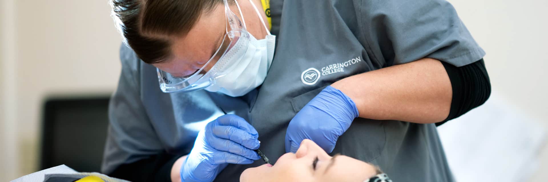 Woman in mask and goggles cleaning female patient's teeth.