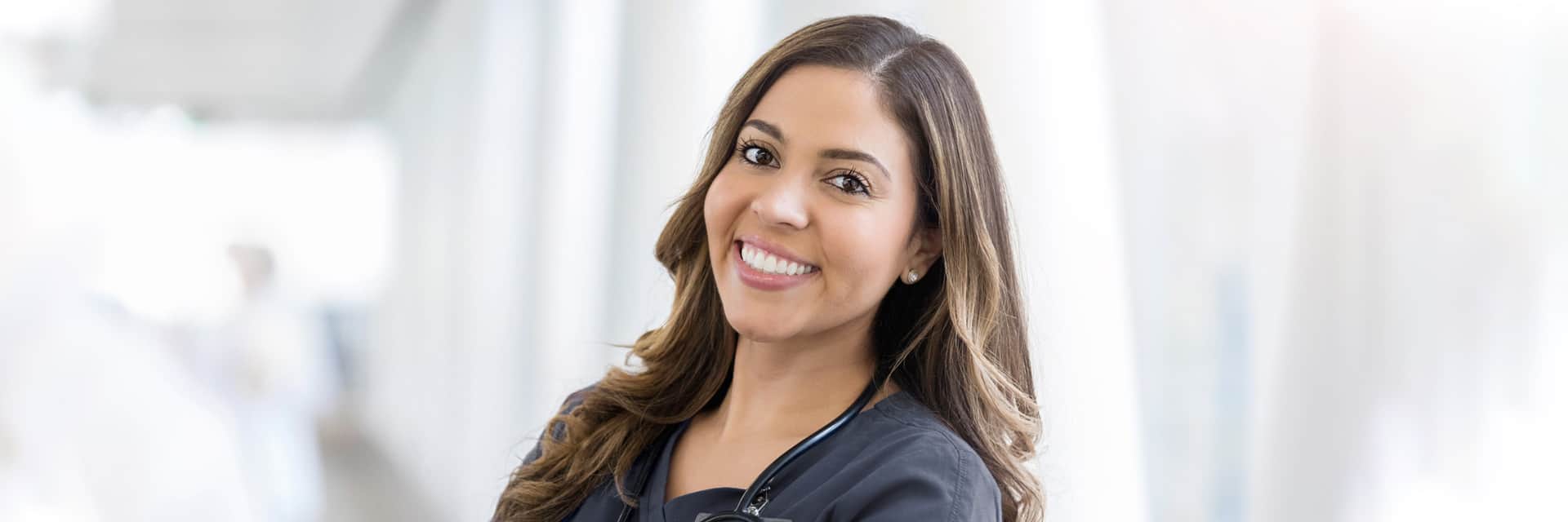 Young woman in dark scrubs with a stethoscope.