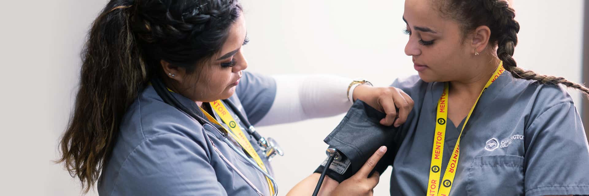 wo young women in scrubs using a blood pressure gauge.