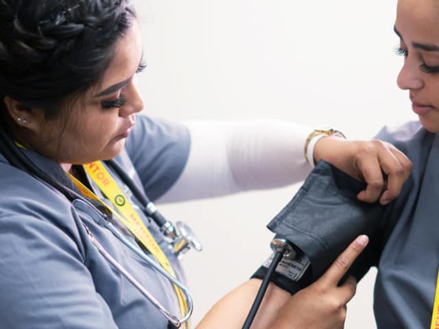 wo young women in scrubs using a blood pressure gauge.