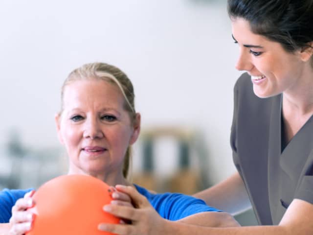 Young woman in scrubs with female patient with exercise ball.