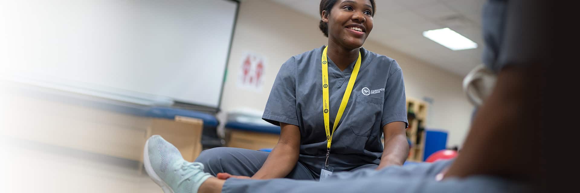 Young woman in scrubs helping patient with leg flexibility.
