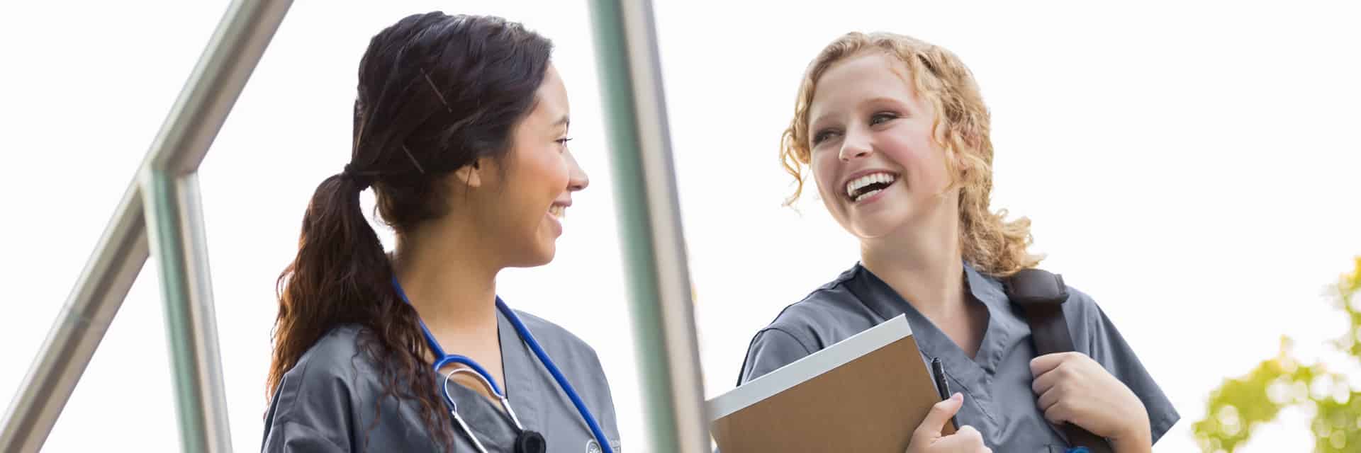 Two young woman in scrubs with stethoscope and notepad.