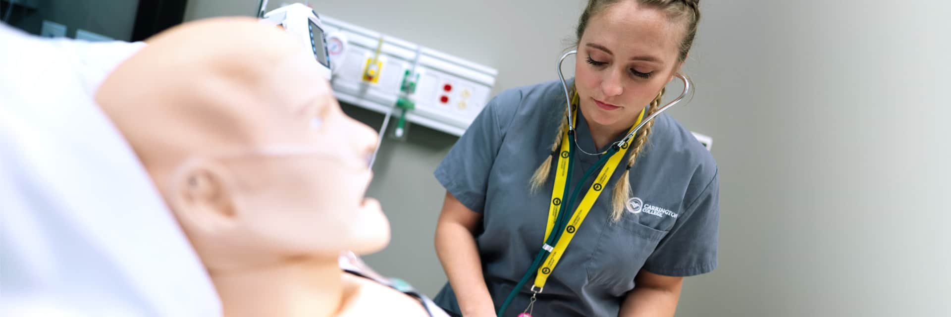 Young woman in scrubs and stethoscope training with dummy patient.