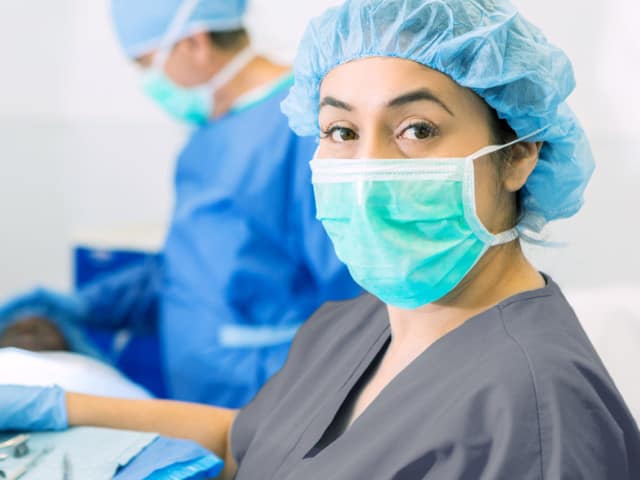 Young woman in scrubs and mask in surgery room.