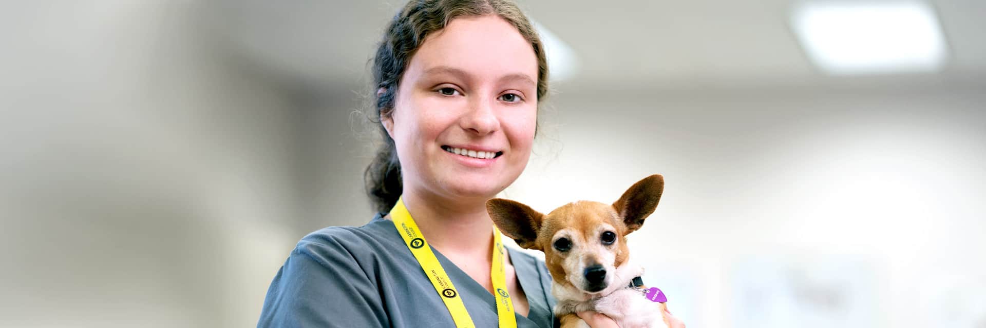 Young woman in scrubs holding small dog.